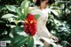 A naked woman standing next to a red flower.