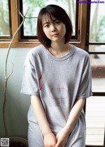 A woman sitting in front of a window wearing a gray shirt.