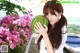 A woman holding a watermelon in front of pink flowers.