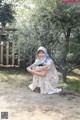 A woman in a white dress sitting under a tree.