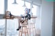 A woman sitting on a stool in front of a window.