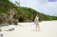 A woman standing on a sandy beach next to a cliff.